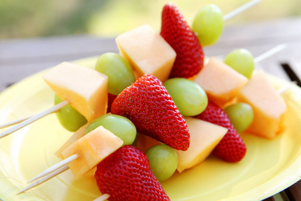 Fruit skewers including cantaloup, strawberry, and grapes, sitting on a plate.