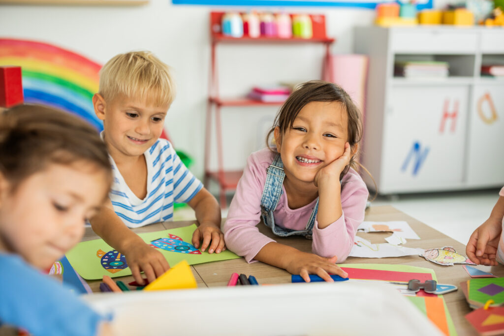 Group of happy little children are sitting on the floor in the kindergarten and playing with toys.