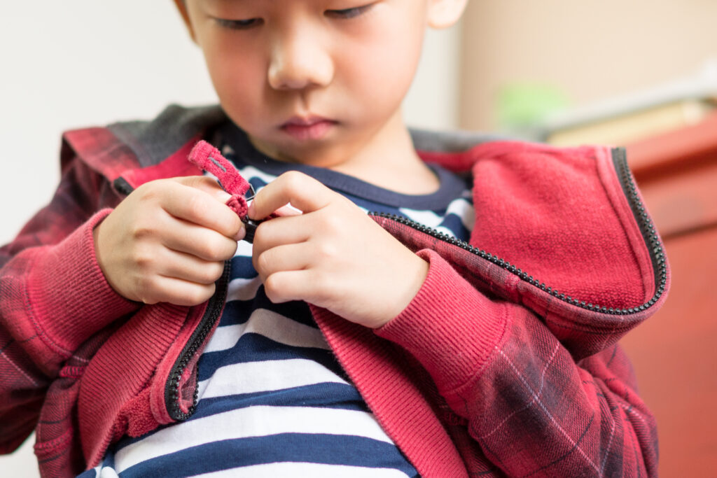 Small cute elementary age Asian boy learning and practicing putting on socks. Child sensory motor, muscle and sensory perception development stage in Montessori education. Self confidence and independence growth.