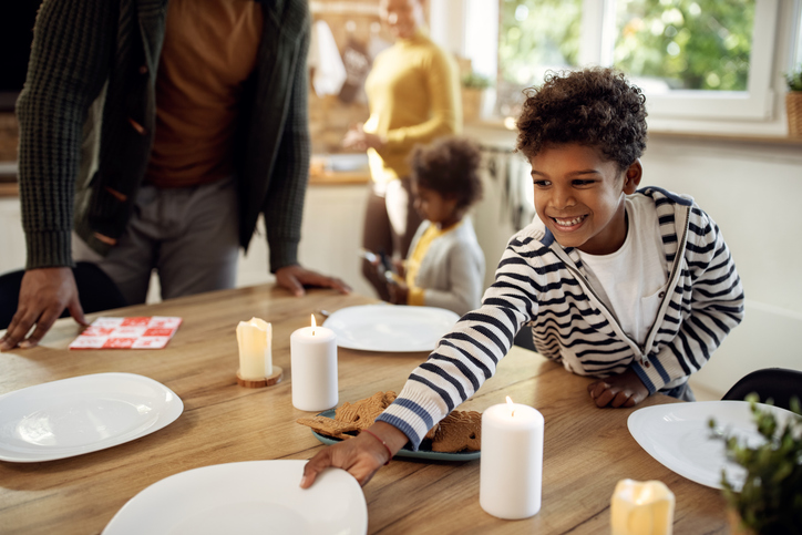 Happy black boy setting dining table while having lunch with his family on holidays.