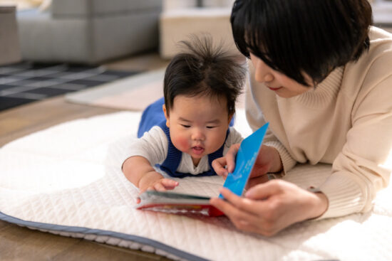 Baby boy and her mother reading a book in living room - close-up